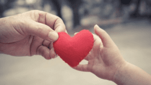 The hand of an adult and the hand of a child hold a felt heart.