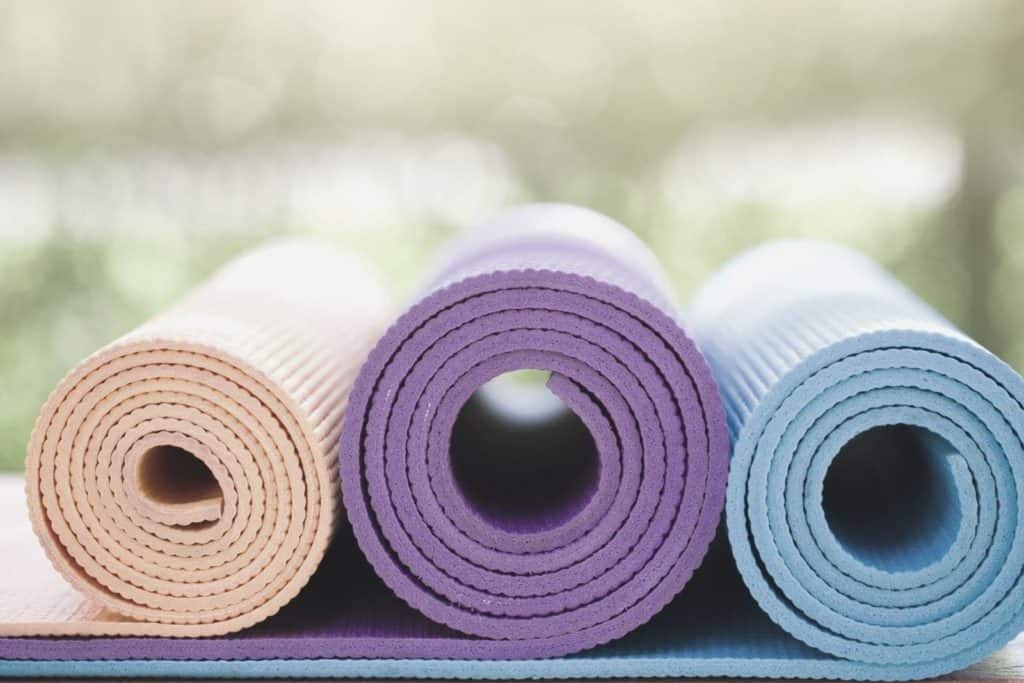three multi colored yoga mats rolled up and lying on the ground side by side