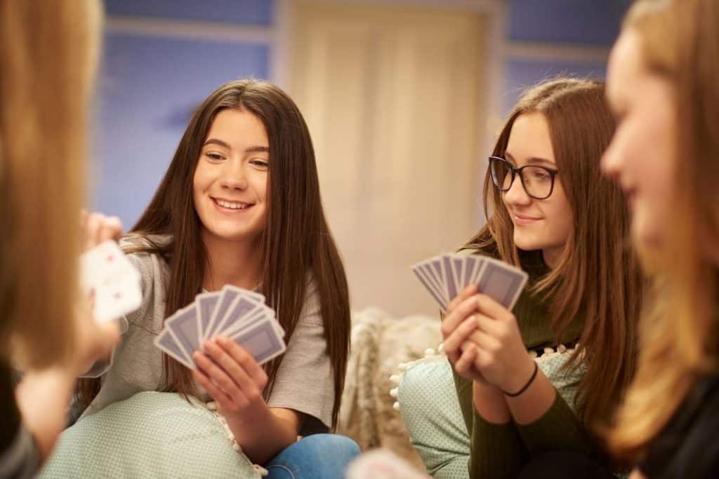 teen girls holding cards as they play a card game