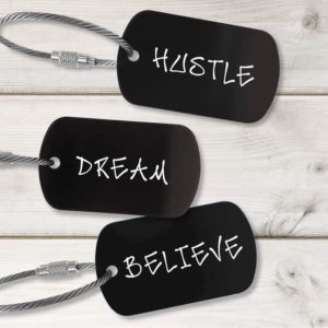 Three black metal tags with silver steel wire cable keychains. Each tag has a different word in white: HUSTLE, DREAM, BELIEVE