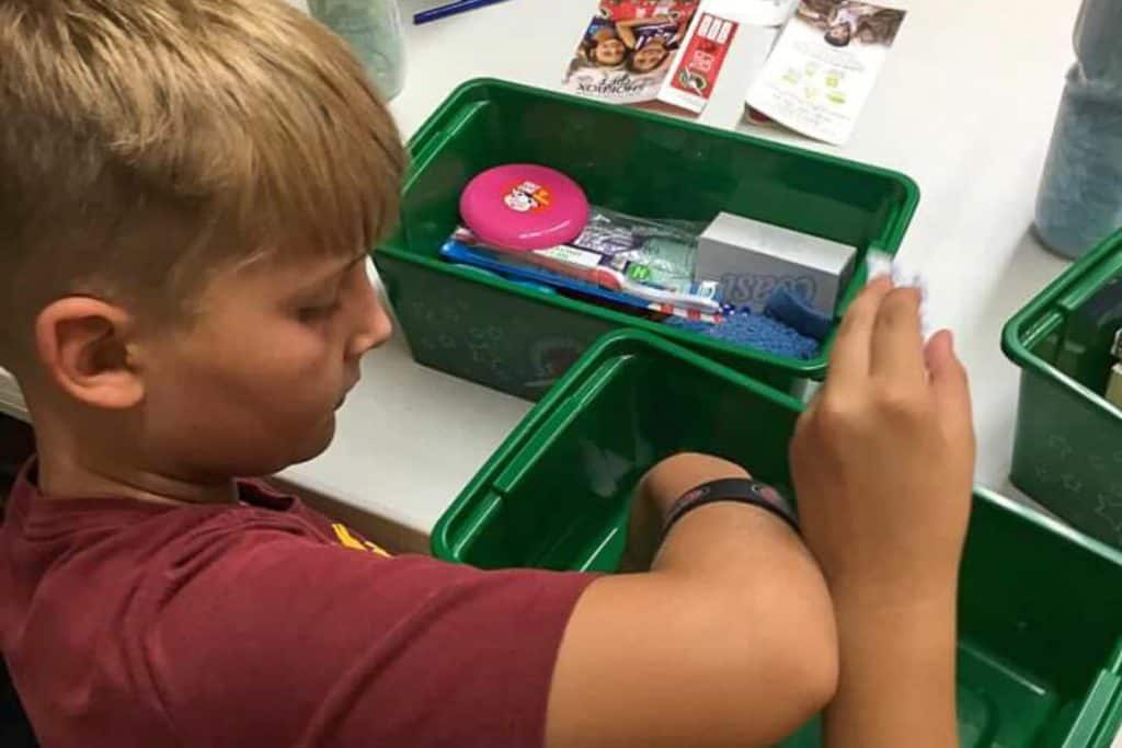 A tween boy putting toys and hygiene items into a plastic green box for Operation Christmas Child.