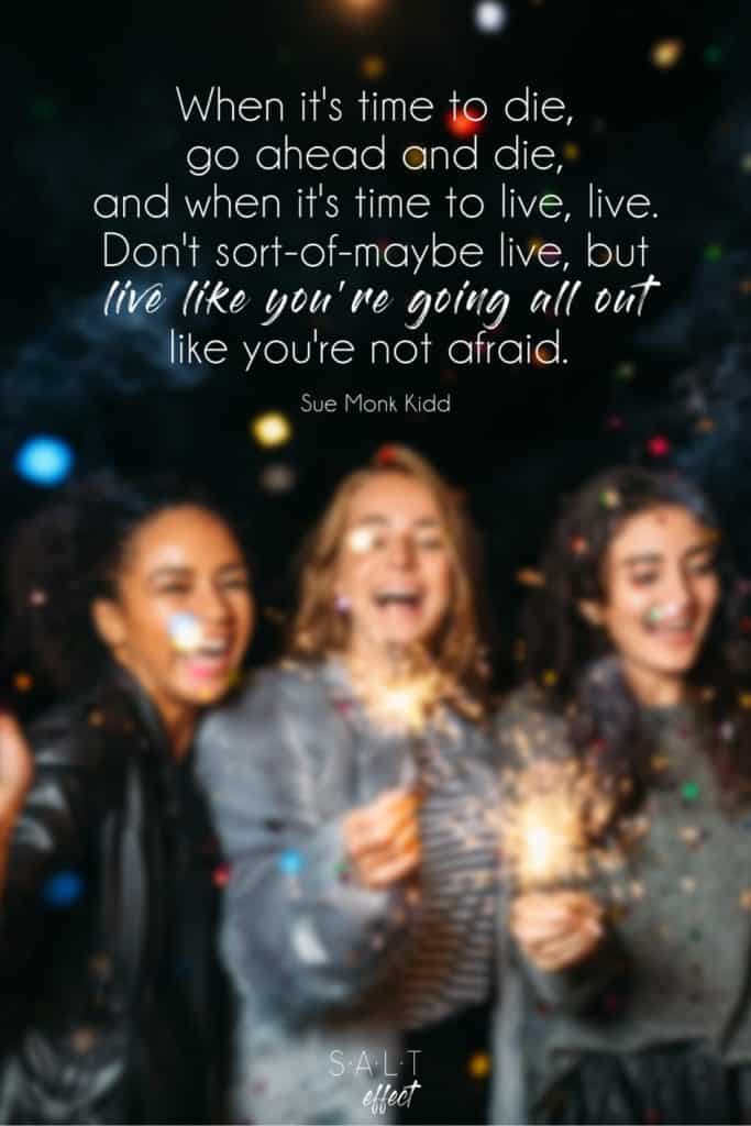 "When it's time to die, go ahead and die, and when it's time to live, live. Don't sort-of-maybe live, but live like you're going all out, like you're not afraid." Quote by Sue Monk Kidd in white text on a black background with a blurred image of three young women laughing and holding sparklers.