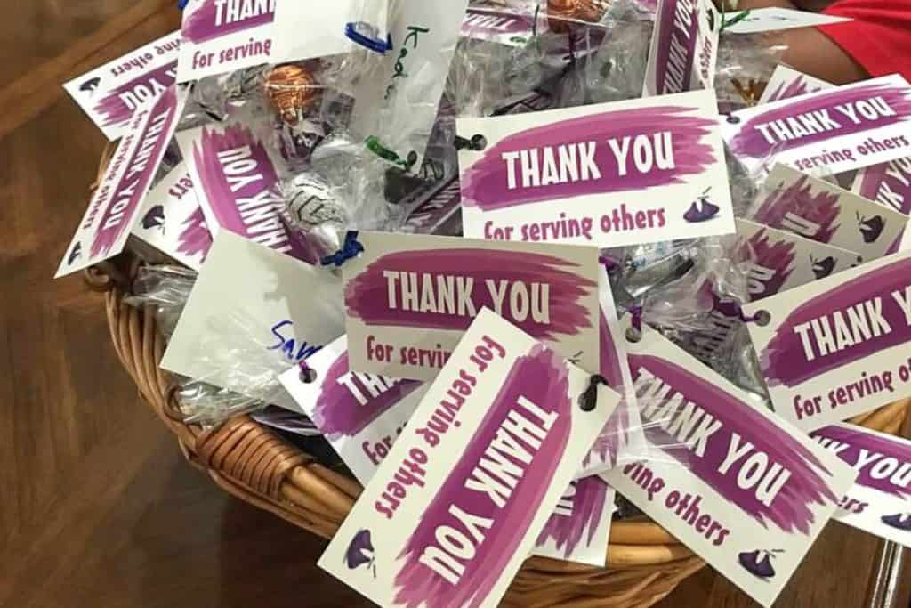 A basket full of small bags of candy with notes that say "thank you for serving others."