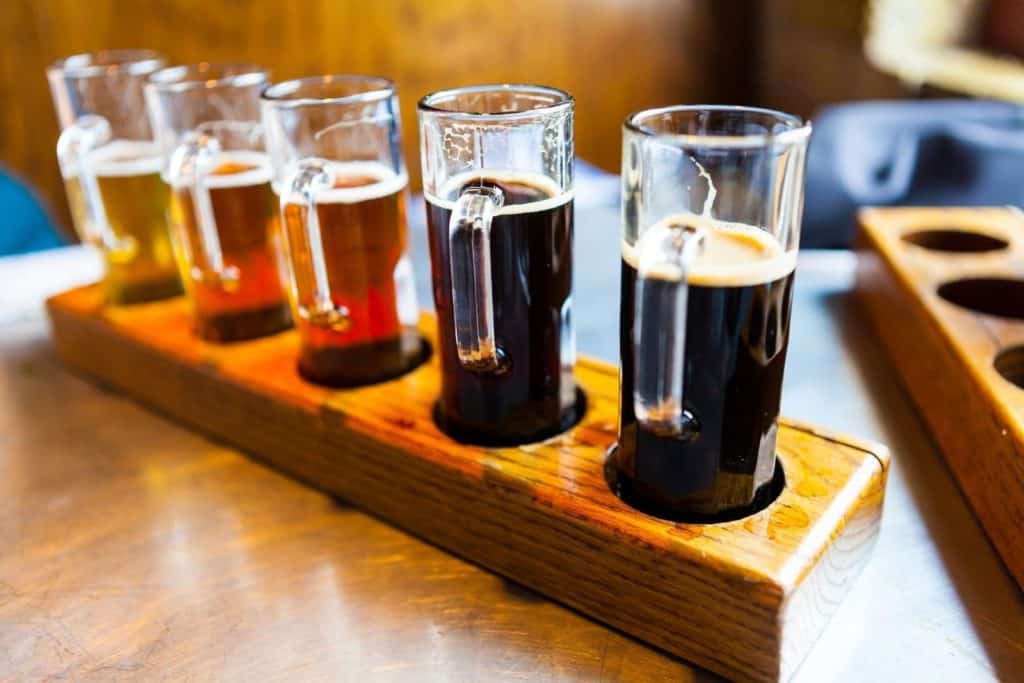 a flight of different colored beers in a wooden holder