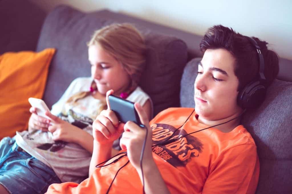 teenage boy and girl sitting on the couch looking at their phoes