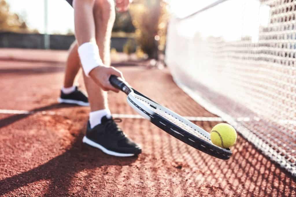 a person picking up a tennis ball with a raquet