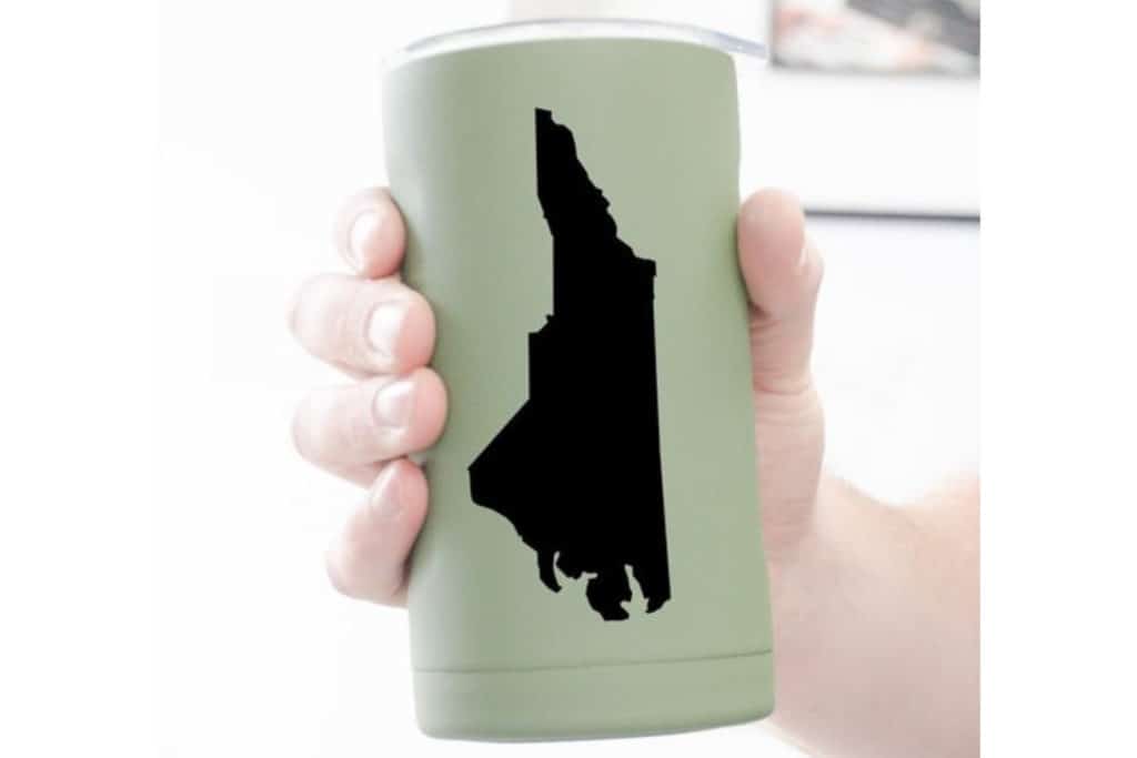 Man's hand holding a sage green can cooler (Hopsulator) with an image of North Carolina in black