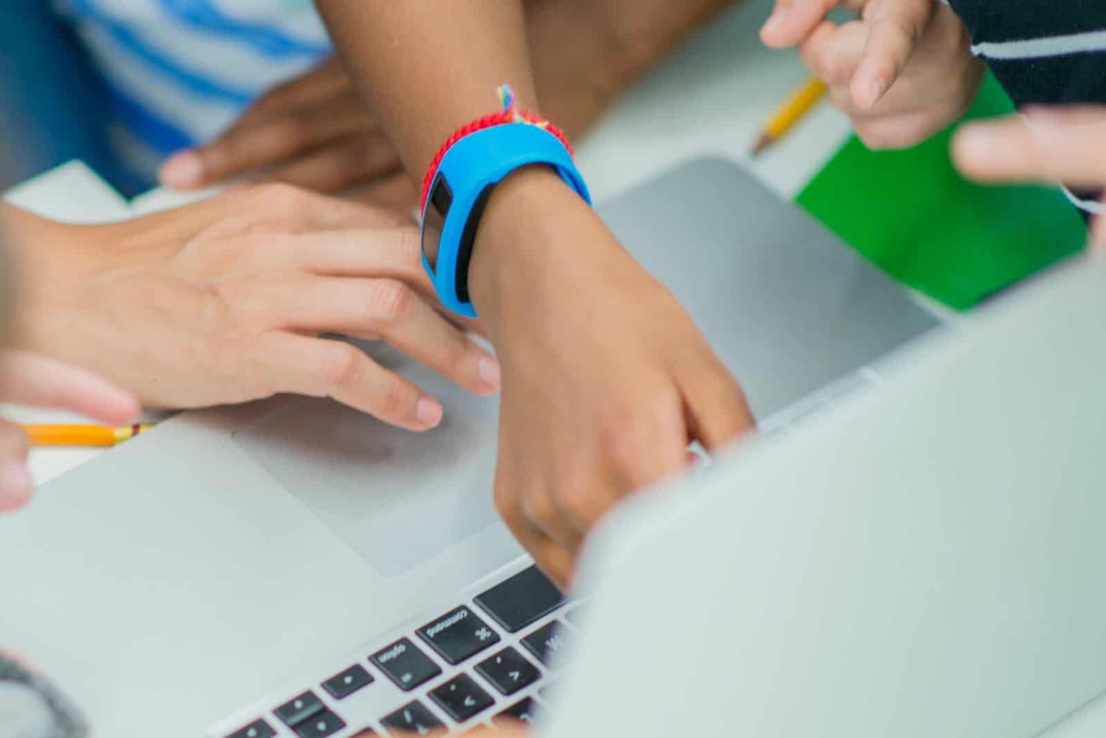 Picture of a tween's wrist wearing a blue smartwatch, pointing at a laptop screen