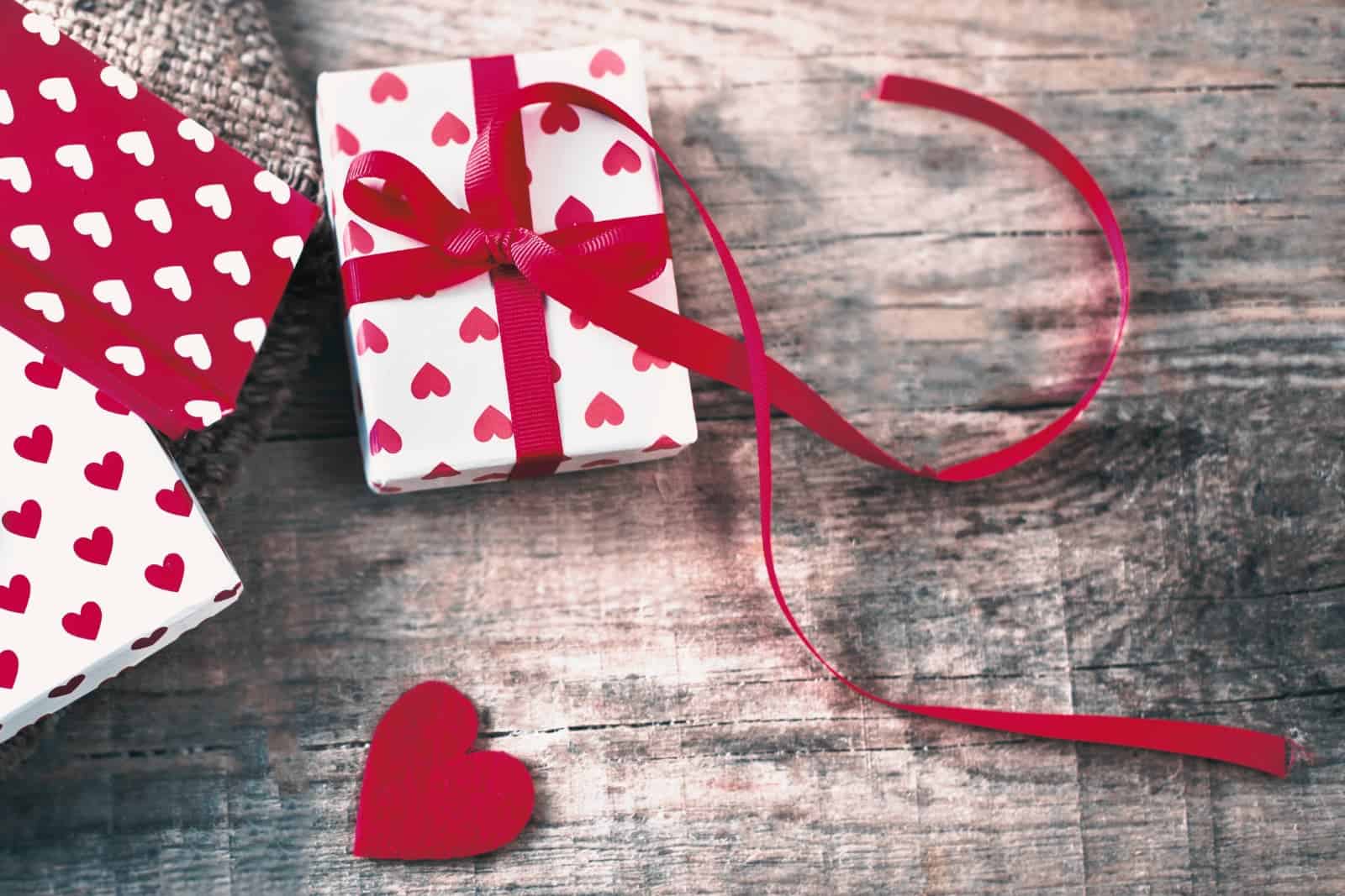 Valentine's gifts wrapped in red and white paper covered with small hearts, on a wood grain background