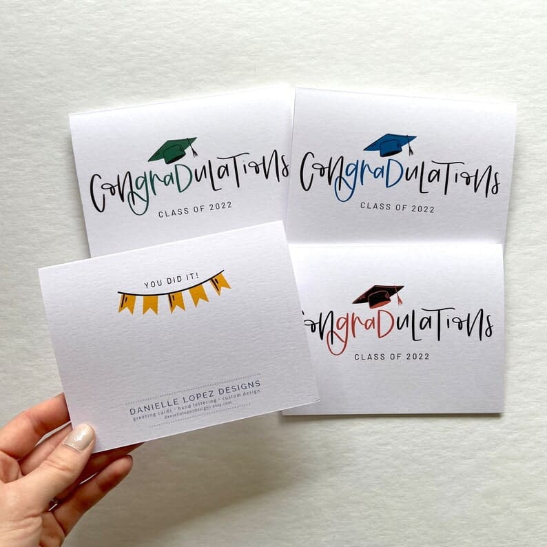 Set of 4 graduation cards for college graduates. "Congradulations" on heavy white cardstock with graduation cap in green, blue and red. Back of card has a yellow banner with the words "you did it!" above it.