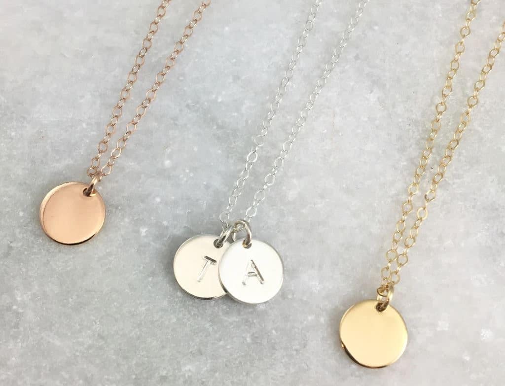 Three necklaces on white cotton batting. Charms are small discs on a dainty chain in rose gold, silver and gold. The silver chain has 2 discs that are hand stamped with T and A.