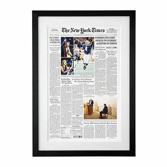 Reprint of the front page of the New York Times. Framed in a black frame. Pictures on the front page are of a football player celebrating on the field, musician on stage, a woman singing, and a man speaking at a podium next to a man sitting on a chair.