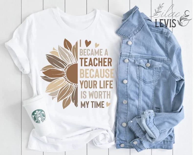 White graphic tee flat lay next to Starbucks cup and denim jacket. Graphic covers the shirt: half of a sunflower in brown tones next to words that say "I became a teacher because your life is worth my time"