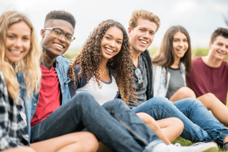 Cover image for Teenage Low Self Esteem post. Six teenagers sitting on the ground, legs out to the right and faces toward the camera. Three girls and three boys in jeans and shorts.