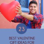 Pinterest pin that says "23 best Valentine gift ideas for teen boys" below an image. Dark haired older teenage boy wearing a red and blue plaid shirt with sleeves rolled up and blue shirt underneath. Holding a heart shaped balloon with extended arms toward camera. Standing in front of a reddish building with blue windows with iron bars.