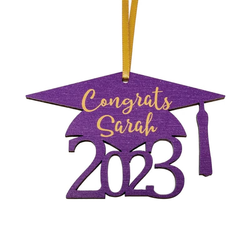 Wooden graduation cap ornament with gold ribbon and 2023 below the cap. Ornament is purple with "Congrats Sarah" in gold on the cap